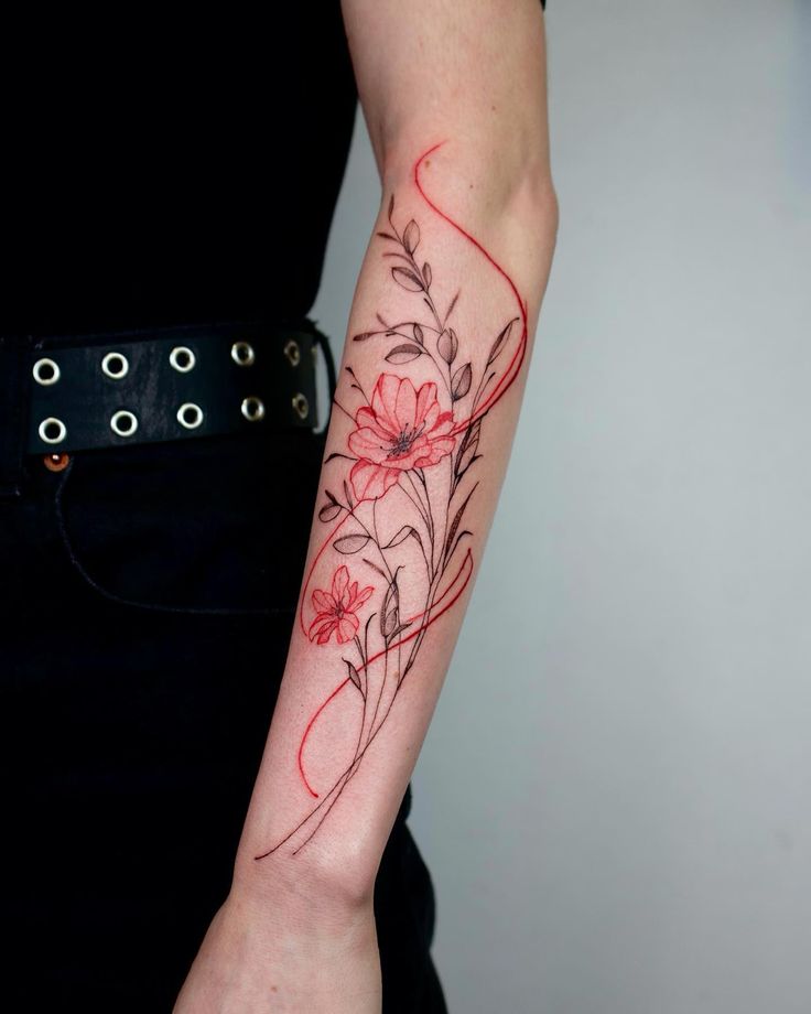 Delicate floral tattoo in red and black ink on forearm, featuring leaves and blossoms. Minimalist tattoo design.