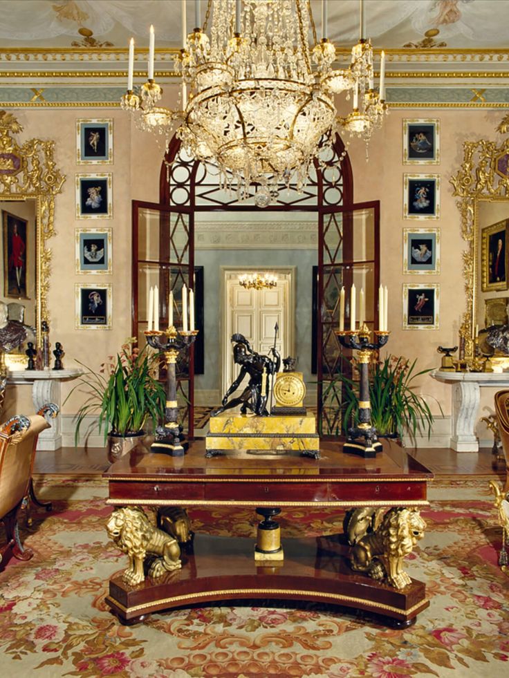 Elegant vintage room with ornate chandelier, decorative table, and classic paintings in luxurious setting.