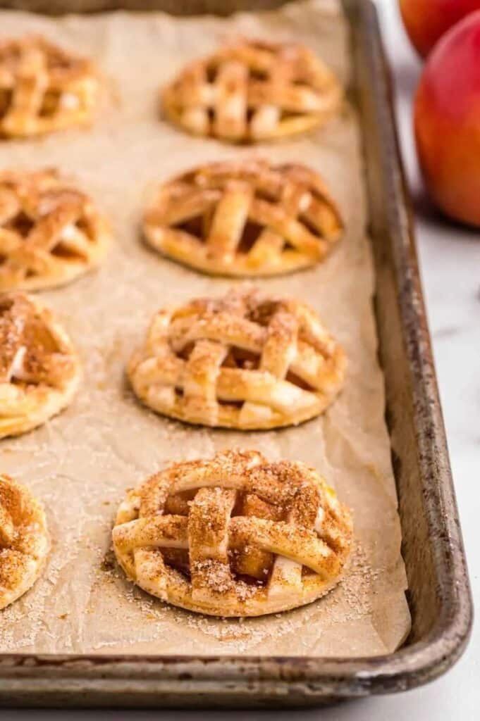 Mini apple pies with lattice crusts on a baking tray, perfect for fall desserts.