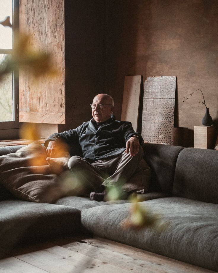 Elderly man relaxing on a modern sofa in a cozy, rustic living room with large window light.