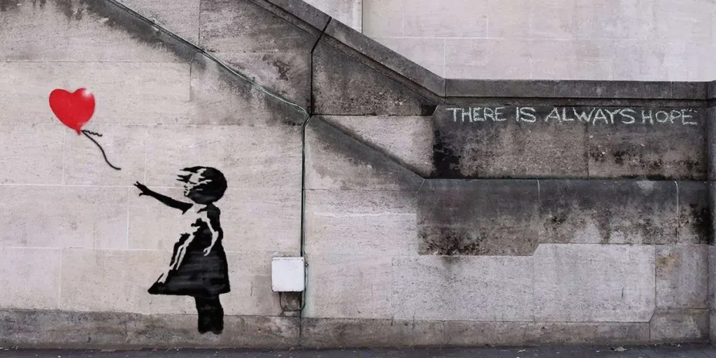 Street art of a girl reaching for a red balloon, with text There is always hope on a concrete wall.