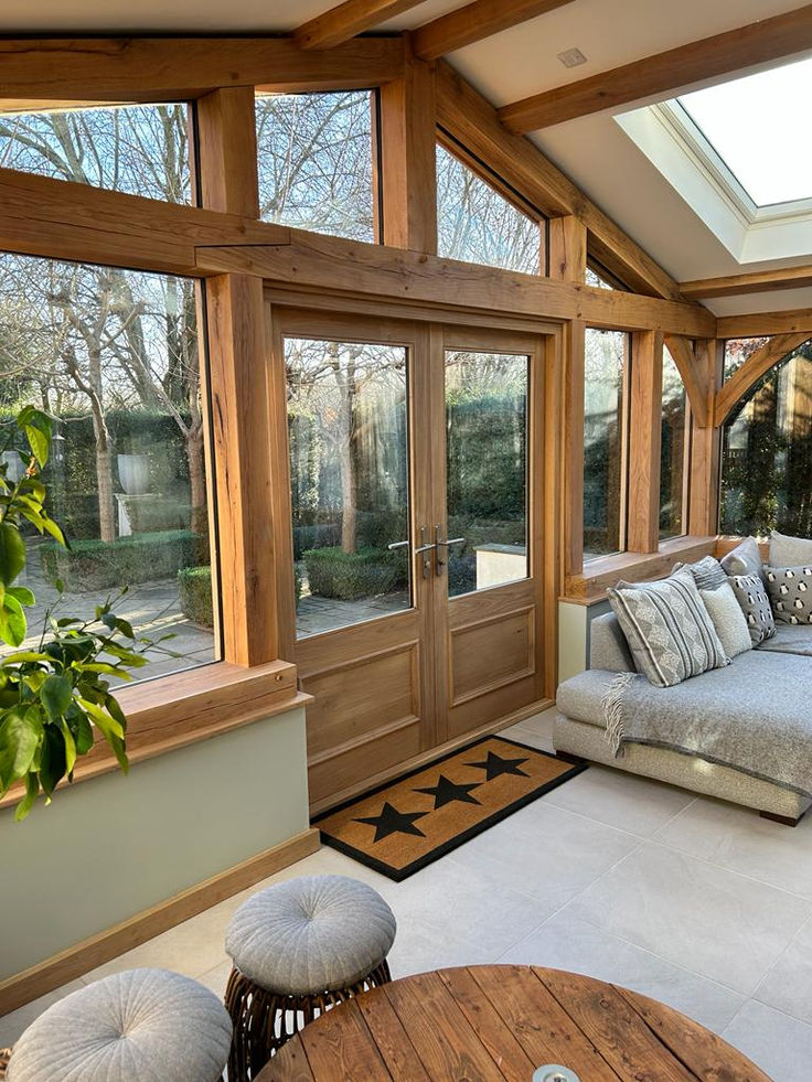 Cozy sunroom with wooden beams, glass doors, gray couch, and skylight, offering a view of the garden.