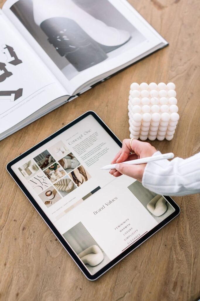 Tablet on wooden desk displaying brand concept, alongside a magazine and decorative cube candle.