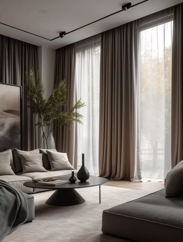 Modern living room with grey sofas, black vases, large windows, and elegant drapes, creating a cozy, minimalist atmosphere.