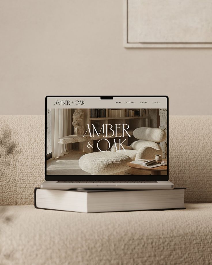 Laptop displaying Amber & Oak website on a cozy, neutral-toned couch with a book underneath.