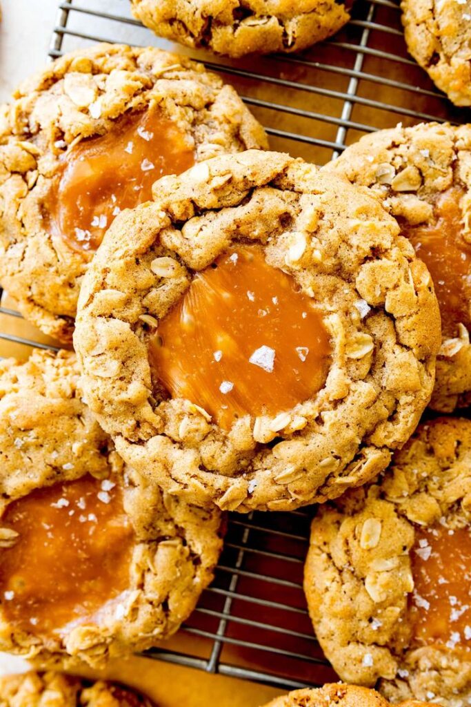 Gourmet salted caramel oatmeal cookies cooling on a wire rack, with a gooey caramel center and flaky salt sprinkles.