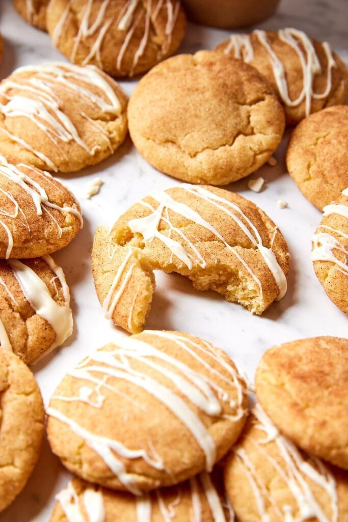 Delicious cinnamon cookies drizzled with white icing on a marble surface, one cookie partially broken.