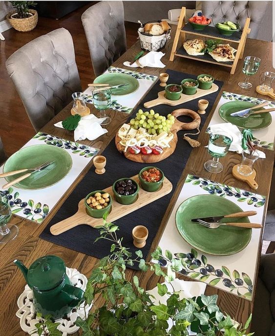 Elegant dining table setup with green plates, wooden boards, assorted appetizers, and decorative greenery.