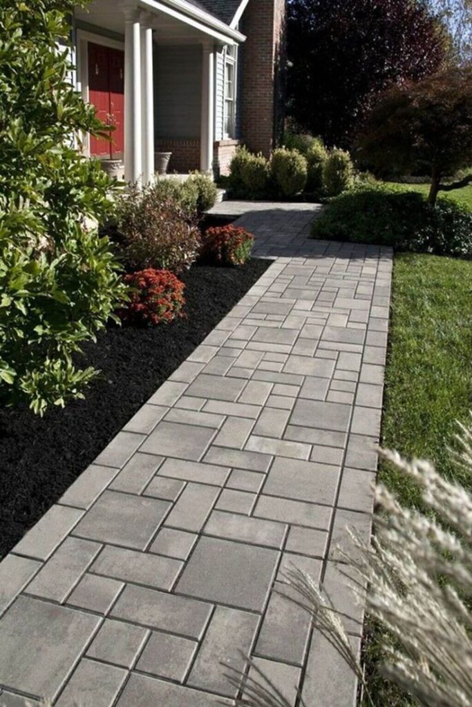 Modern stone walkway leading to a home's entrance, surrounded by lush gardens and vibrant greenery.