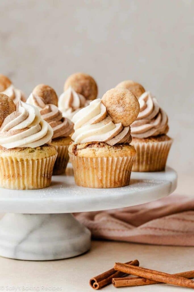 Delicious snickerdoodle cupcakes topped with frosting and cookies on a marble stand.