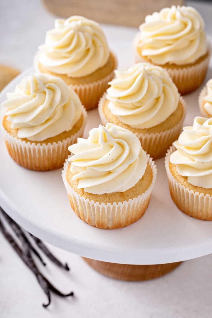 Vanilla cupcakes with creamy frosting displayed on a white cake stand, perfect for dessert lovers.