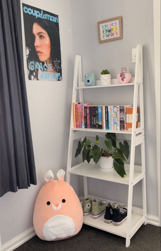 Cozy room corner with a ladder shelf, books, plant, camera, plush toy, and shoes for a stylish decor setup.