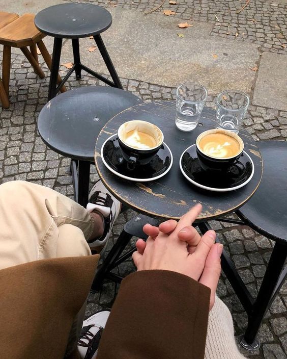 Couple holding hands at outdoor cafe table with two cappuccinos.