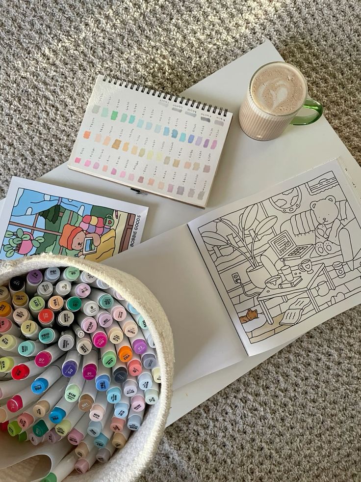 Art supplies on a table: markers, coloring books, color palette, and a cup of coffee, ready for a creative session.