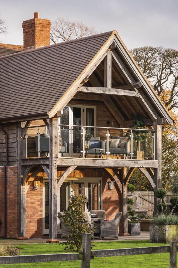 Rustic wooden house with a balcony, cozy chairs, and a green garden, perfect for nature-inspired living.