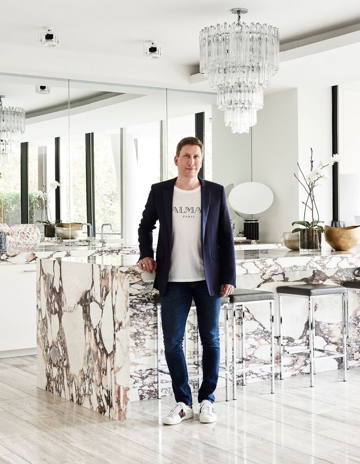 Man in modern kitchen with marble countertops and elegant decor, wearing casual outfit with blazer.