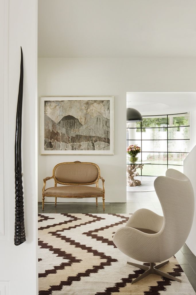 Modern living room with a patterned rug, elegant chairs, and a landscape painting on the wall.