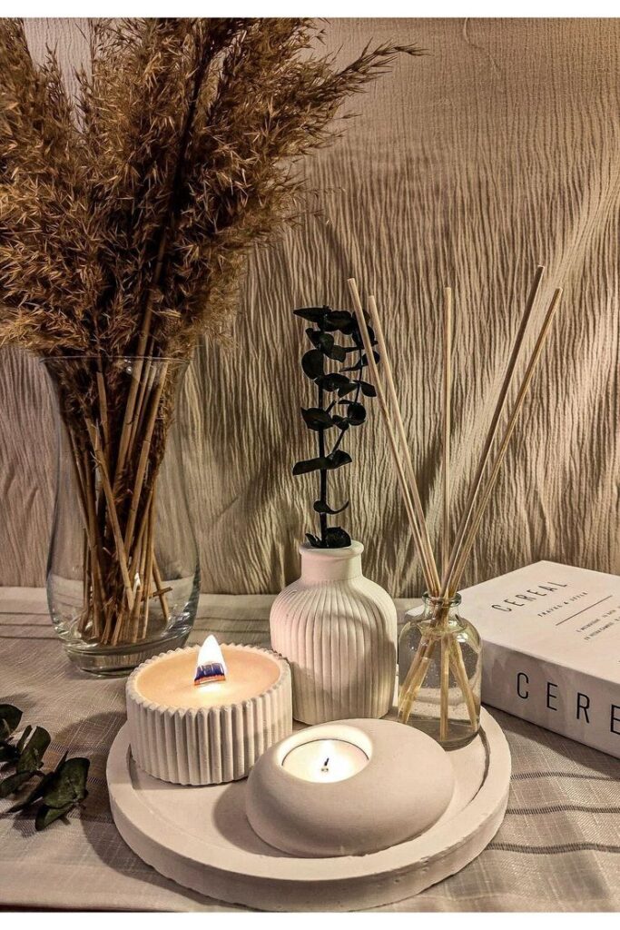 Cozy decor with candles, reed diffuser, and dried grass in vases on a table for a serene ambiance.