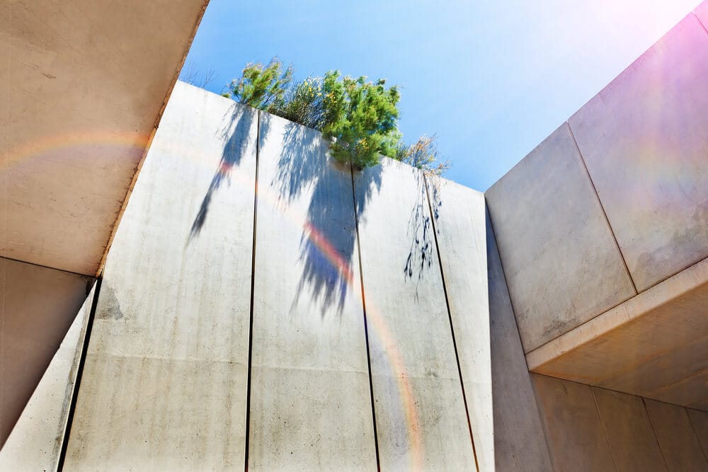 Concrete walls with rainbow reflection and trees under a clear blue sky.