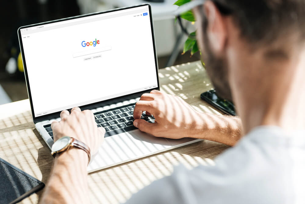 Person searching on Google using a laptop in a bright, sunny workspace.