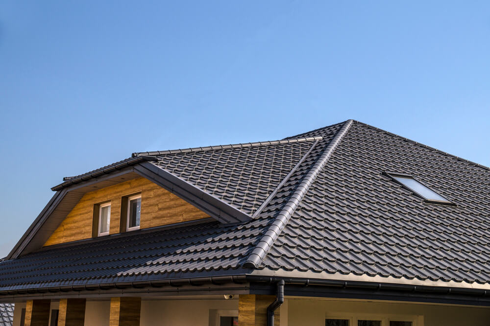 Modern house with a dark gray metal roof, skylight, and wooden paneling under a clear blue sky.