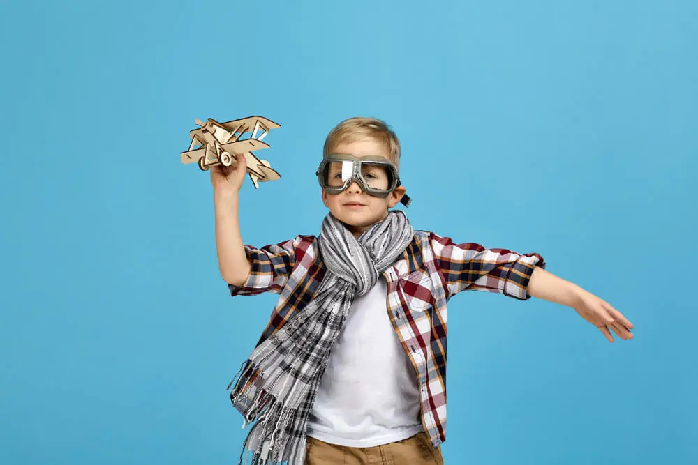Depositphotos_440060386_S 1 Child dressed as pilot with toy airplane against blue background, embodying imagination and adventure. | Sky Rye Design Child dressed as pilot with toy airplane against blue background, embodying imagination and adventure.