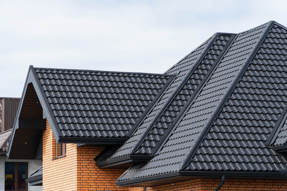 Modern house with sleek black metal roof and brick walls under a cloudy sky.