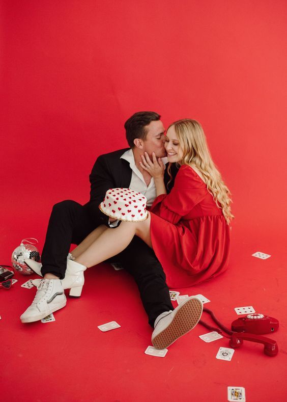 A couple in love sitting on a red background with playing cards and a heart-patterned hat.