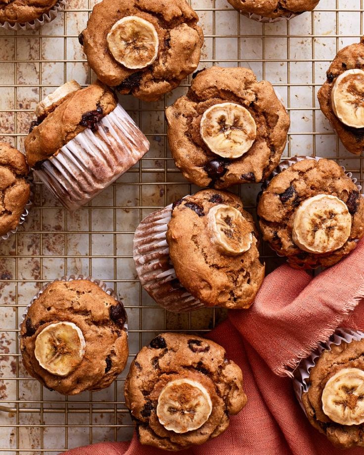 Freshly baked banana chocolate muffins cooling on a rack, topped with banana slices and a hint of chocolate chips.