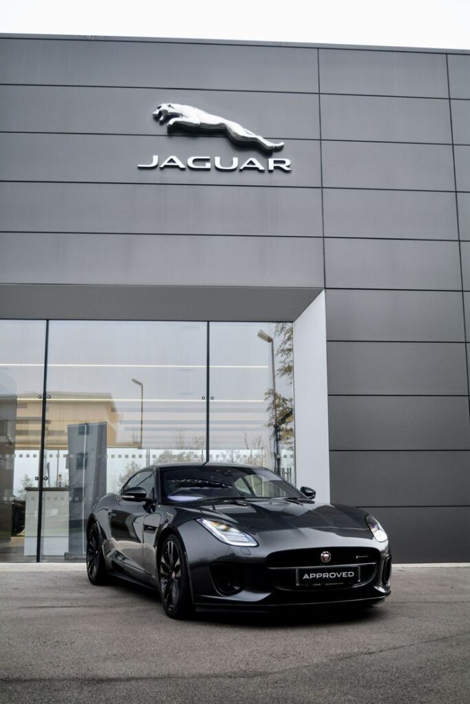 Sleek black Jaguar sports car parked in front of the Jaguar showroom building with logo.