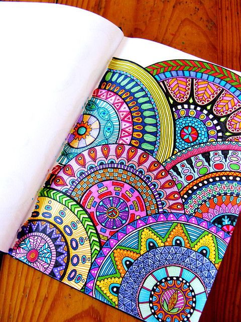 Colorful mandala designs in an open coloring book on a wooden table, showcasing intricate patterns and vibrant hues.