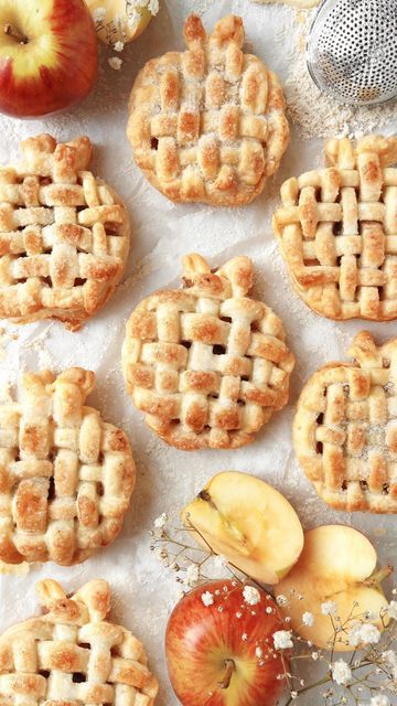 Mini lattice apple pies and fresh apples on a light background, highlighting a perfect autumn dessert setting.