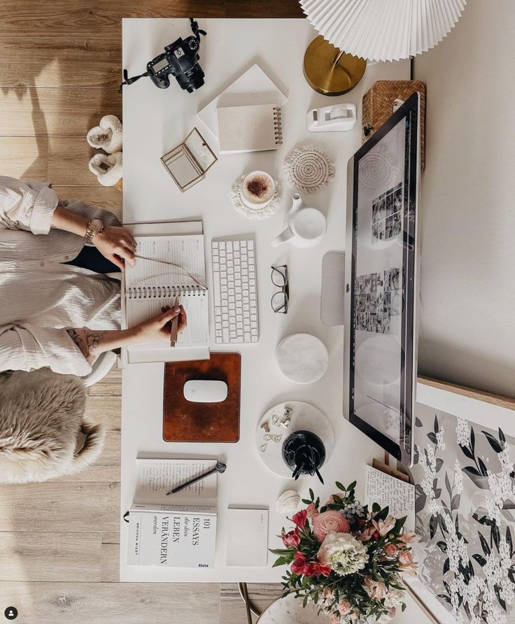 Laptop workspace with notebook, camera, coffee, and flowers on a desk, offering a cozy and productive atmosphere.