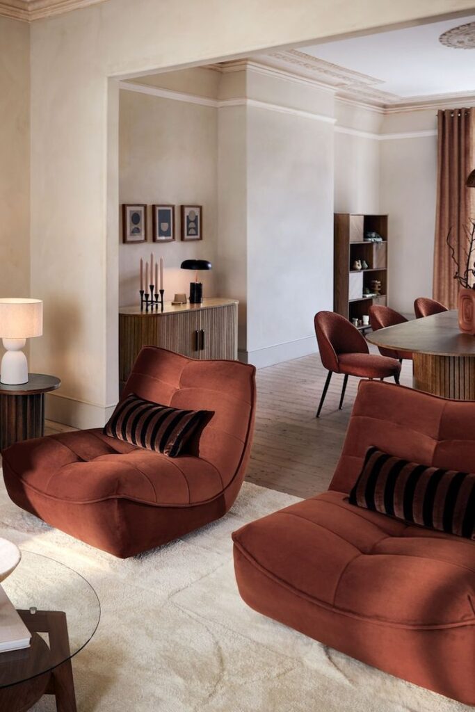 Modern living room with rust-colored chairs, elegant decor, and soft lighting, creating a warm and inviting atmosphere.