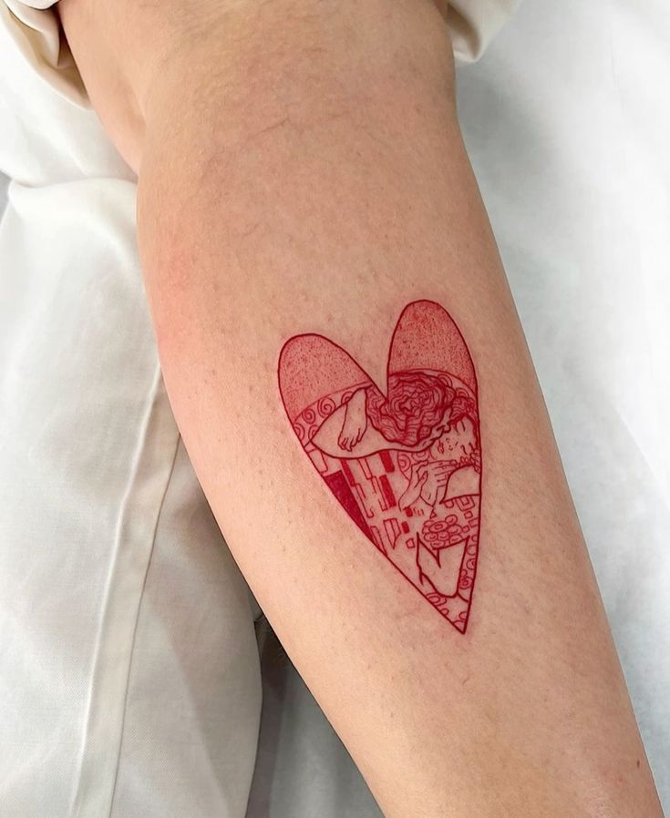 Heart-shaped tattoo on arm featuring intricate red line art of a couple, minimalistic design on light skin.