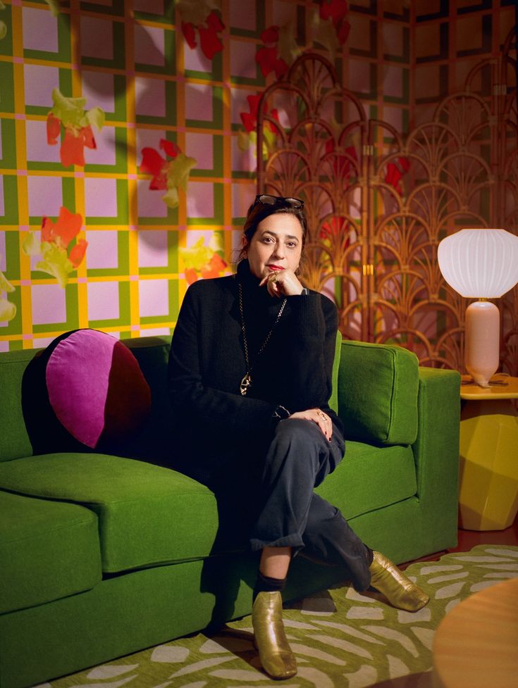 Person sitting on a green couch in a colorful room with floral decor, next to a decorative lamp.