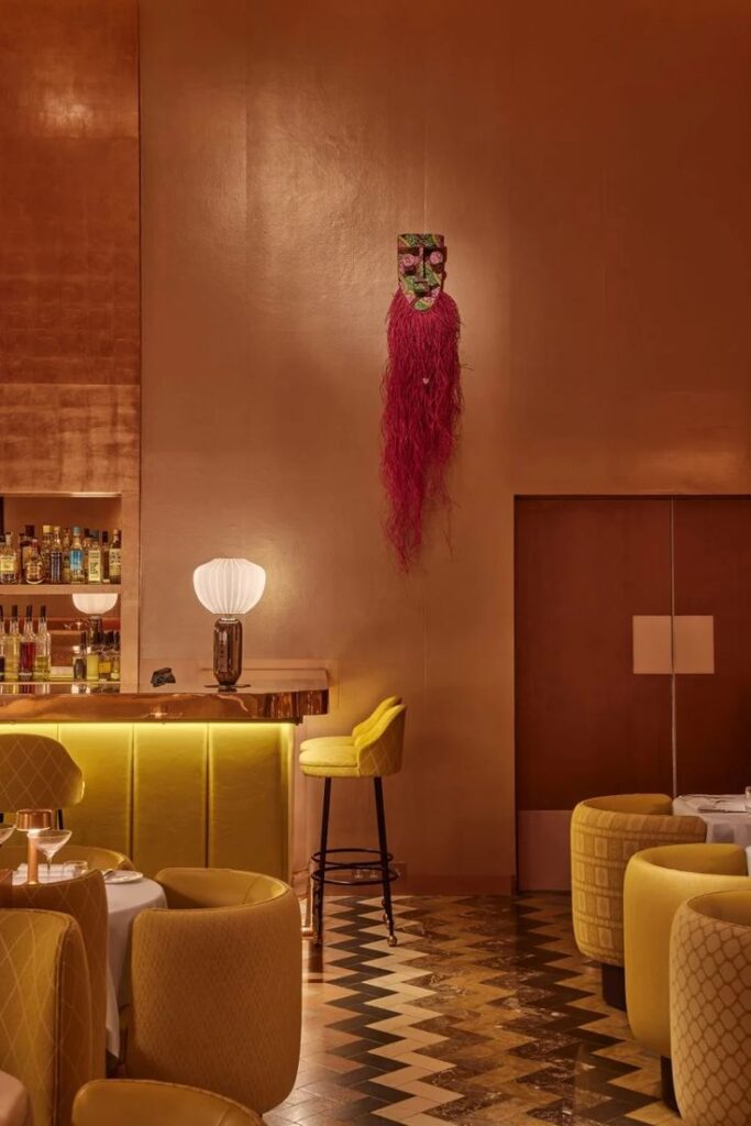 Stylish lounge with yellow seating, elegant bar, and artistic wall decor, creating a warm, chic ambiance.