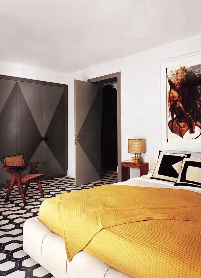 Modern bedroom with yellow bedding, geometric flooring, abstract art, and dark wardrobe doors. Cozy and stylish decor.