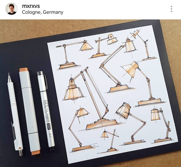 Sketchbook page with anglepoise lamp designs, markers, and pen on a table.