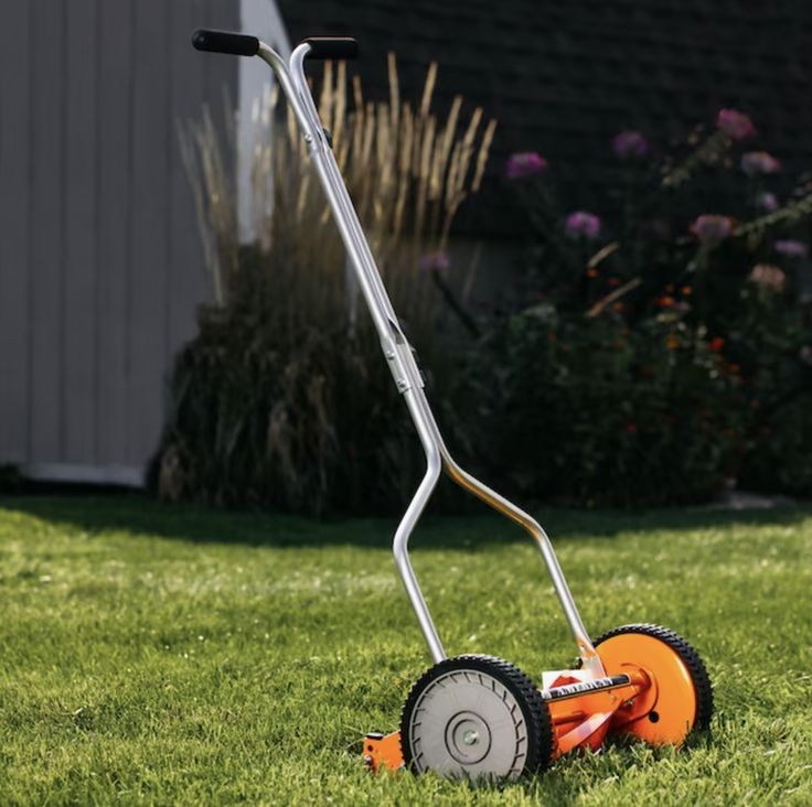 Manual reel lawn mower on green grass in a sunny garden setting.