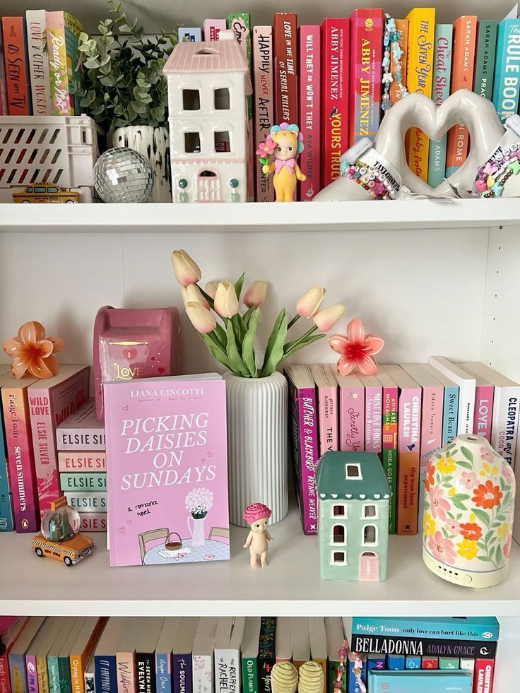 Colorful bookshelf with romance novels, decor, and tulips in a vase for a cozy reading nook vibe.