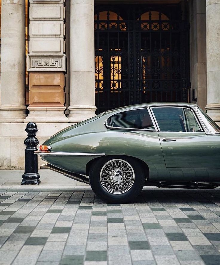 Classic green car parked near ornate building facade with columns. Vintage design and elegant architecture.