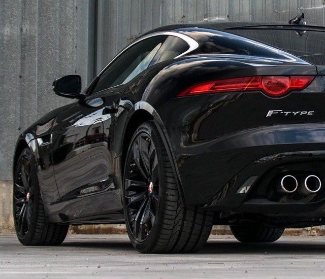 Sleek black sports car with dual exhausts parked in front of an industrial building.