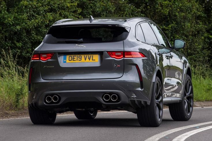 Grey SUV driving on a curved road near greenery. License plate reads OE19 VVL, showcasing sporty design and twin exhausts.