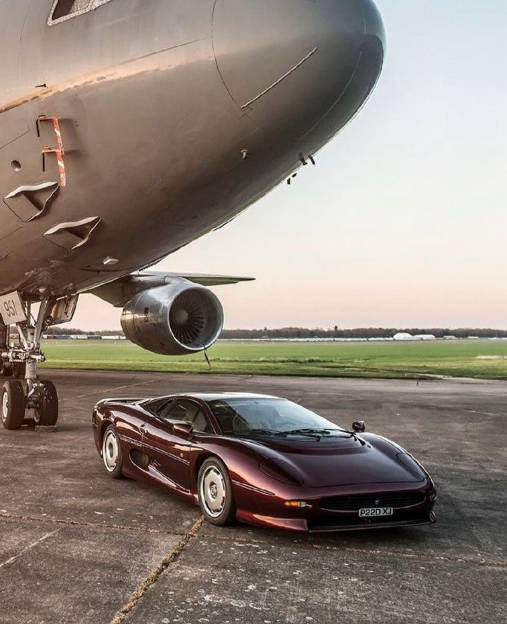 Luxury sports car parked under aircraft on runway at sunset.