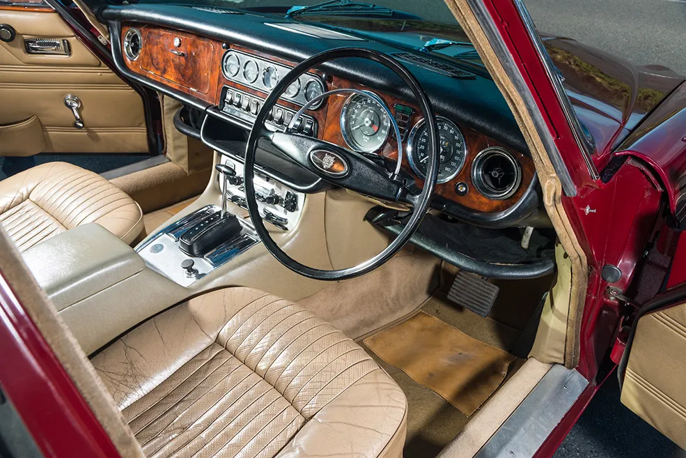 Vintage car interior with classic leather seats, wooden dashboard, and analog gauges.