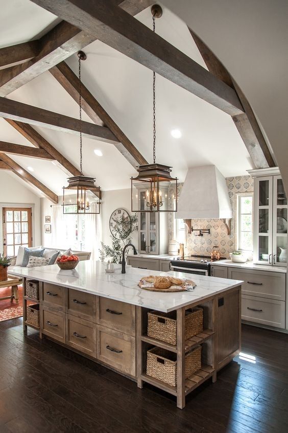 Rustic kitchen with exposed beams, island, modern appliances, and ample natural light in a cozy setting.