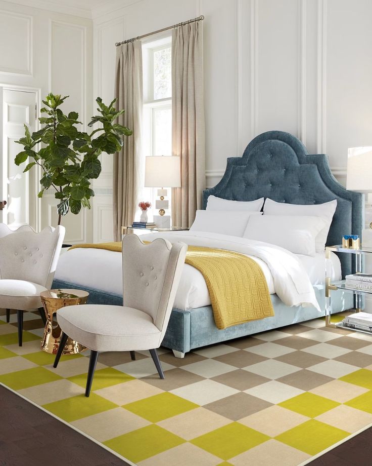 Stylish bedroom with blue velvet bed, yellow accents, checkered rug, and elegant chairs under soft natural light.