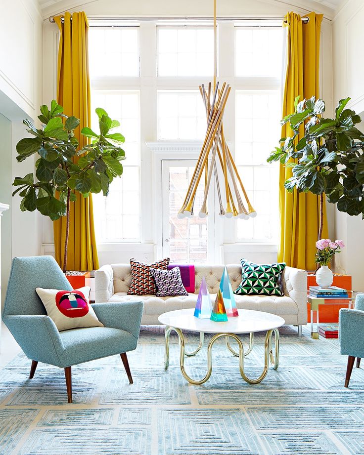 Bright living room with yellow curtains, modern chandelier, colorful pillows, and a mid-century blue armchair.