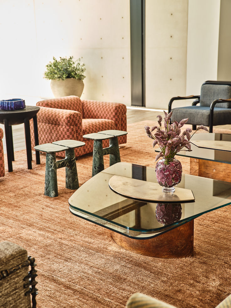 Modern living room with stylish furniture, glass coffee table, patterned couches, and decorative plant arrangement.